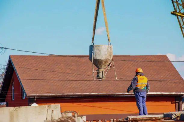 Photo of Construction of a bypass road in the industrial area. Builder worker takes the load with concrete from the boom of the crane