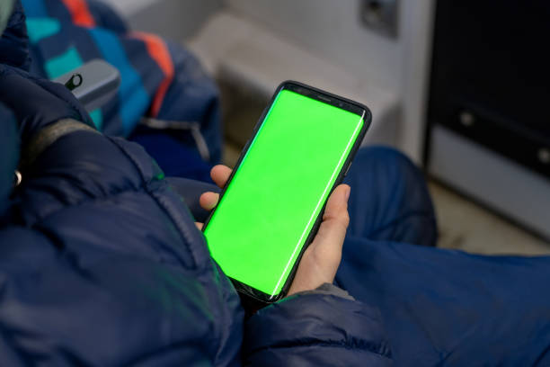 Back view of kid watch smart phone with green screen and browsing online in train. Mock up for watching content on cell phone. Blank digital phone in hand of boy sitting indoors in public transport stock photo