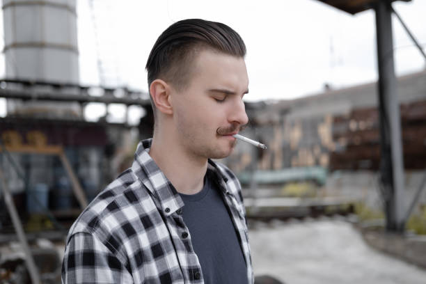 istock young handsome man with mustache in checkered black and white shirt smoking a cigarette outside. bad habit 1388443687