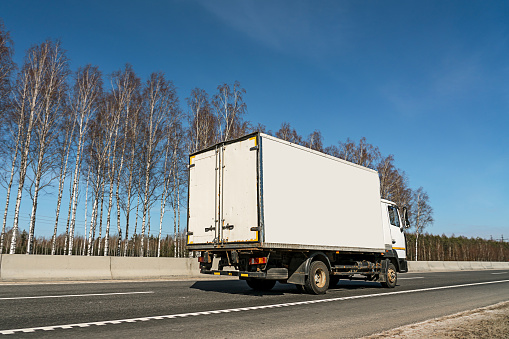Small delivery truck with empty board for mockup space driving on asphalt road of freeway under clear blue sky