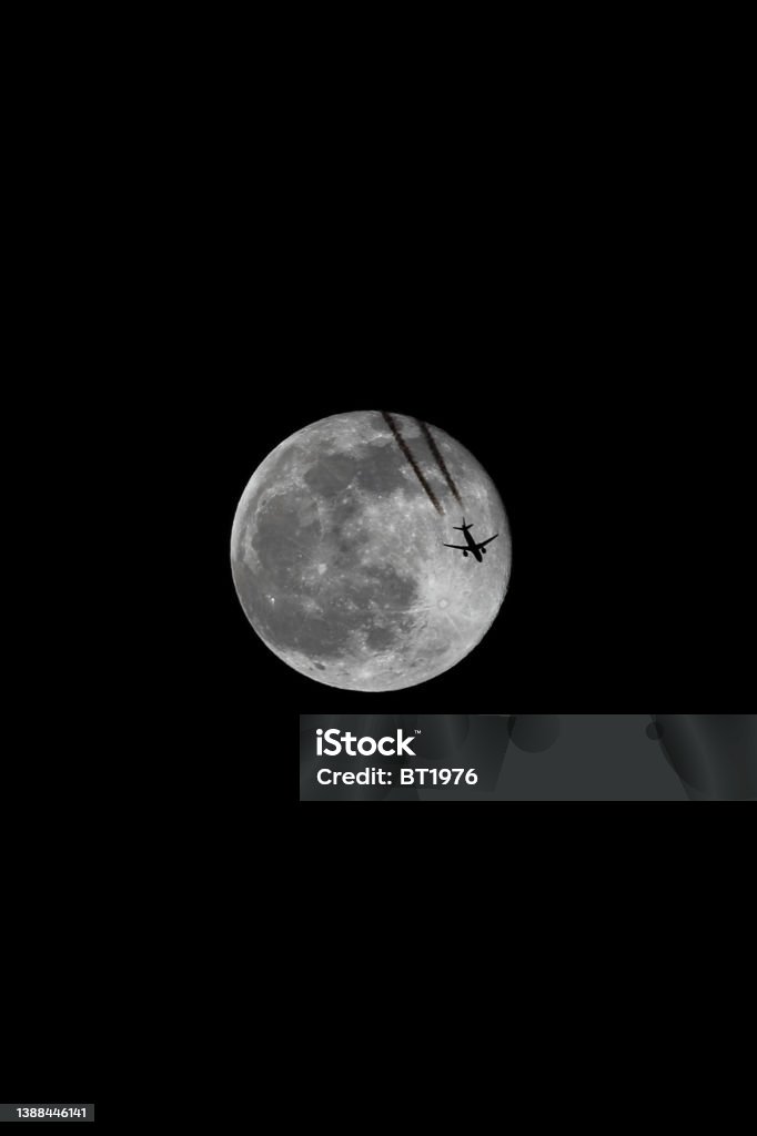 A Jet Flying Under a Full Moon at Night, Color Image Airplane Ticket Stock Photo