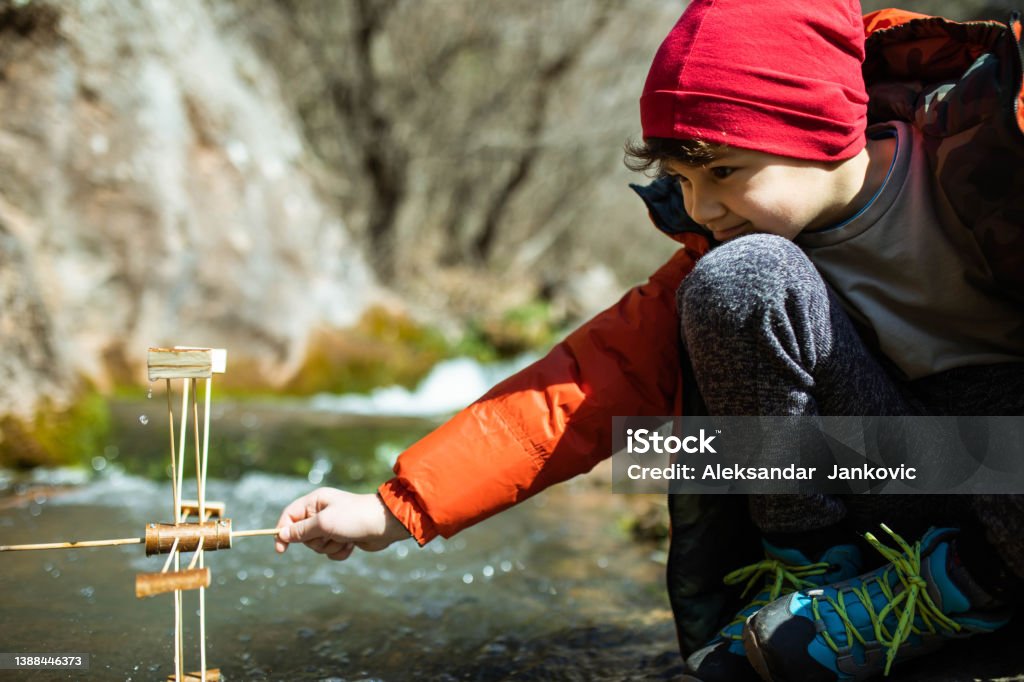 A kid learning about sustainable energy A cute young boy is holding a water wheel in a mountain stream and learning about sustainable energy Water Wheel Stock Photo