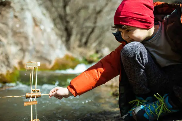 A cute young boy is holding a water wheel in a mountain stream and learning about sustainable energy
