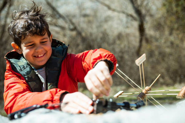 A cute boy is smiling happily while making a waterwheel outdoors with his concentration face on
