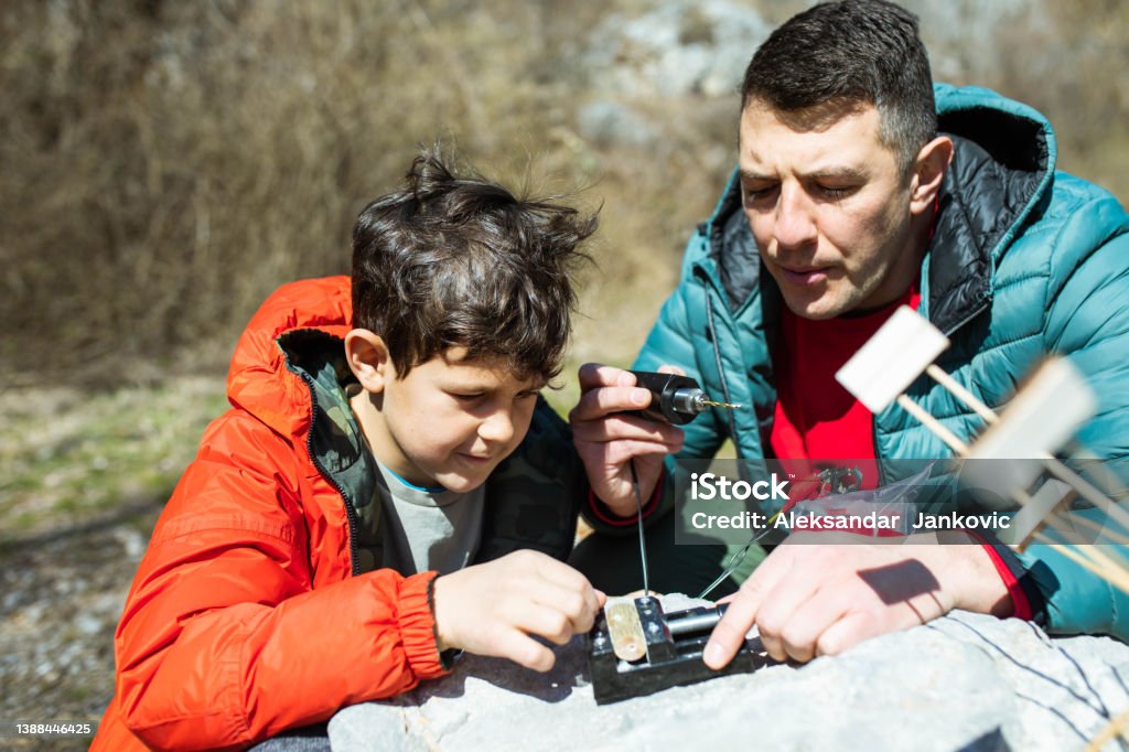 Crafty father and son making a waterwheel outdoors A cute boy is learning about sustainable energy by making a waterwheel outdoors with his dad Building - Activity Stock Photo