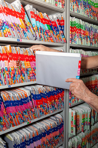 Unrecognizable person is adding a medical file to the hundreds on shelves in a medical records room.