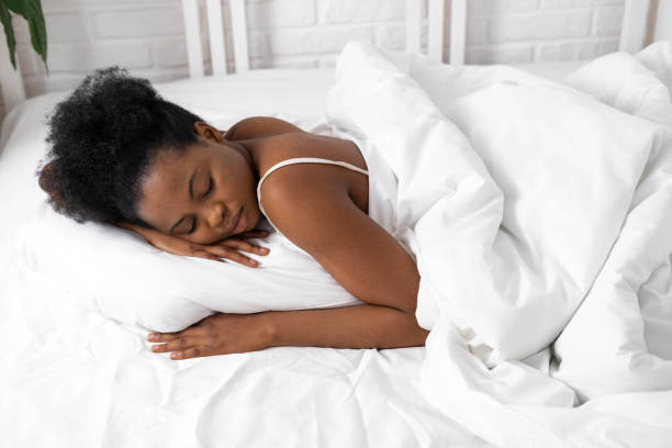 istock African American woman with hands under cheek sleeping in bed with white bedding 1388447729