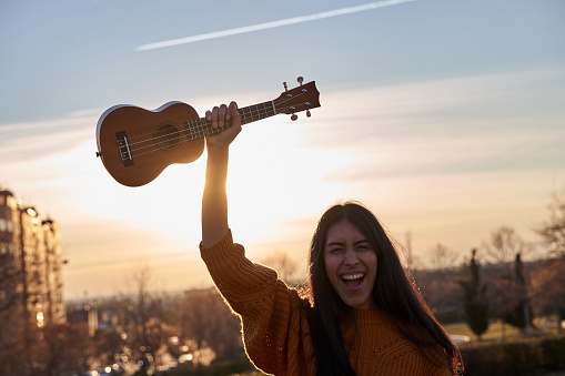 young Latin woman screaming with a ukulele above her head. music concept and leisure time activities