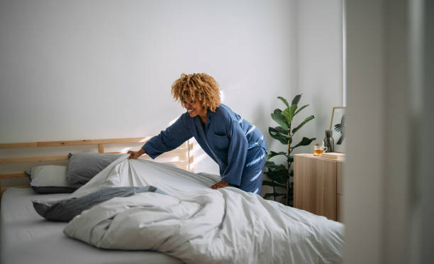 Beautiful Woman Making her Bed in the Morning Smiling African American woman in pajamas making bed after waking up in her bedroom. preparation stock pictures, royalty-free photos & images