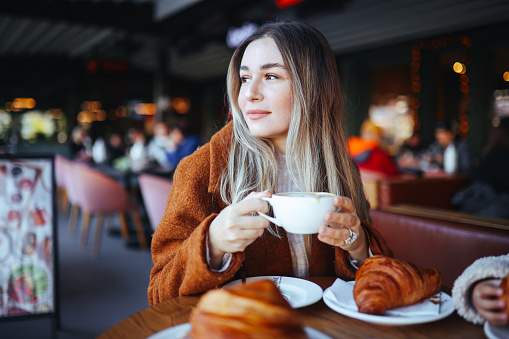 Happy young woman having cafe latte and croissant in cafe