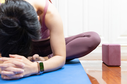 A healthy asian woman doing yoga child pose stretching her back and upper body on the mat in front of a tablet computer. Exercise, Online course, Trends, Workout, Woman health, Home, Relax, Technoloy, Active lifestyle