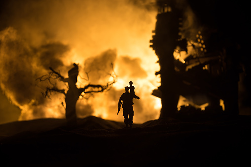 Silhouette soldier carrying little boy on his shoulder from fire. Rescue savior concept. Man moving out with little boy from burned out city destroyed in war. Selective focus