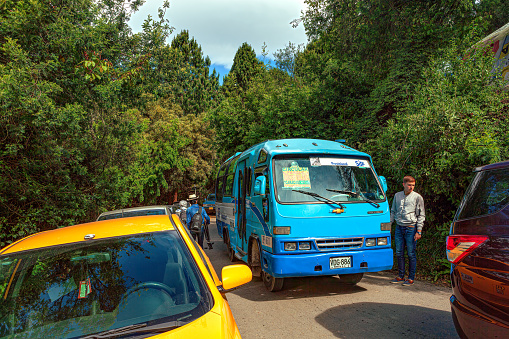 Bogotá, Colombia - July 16, 2017: Cars and buses parked randomly by the roadside create a traffic jam for upcoming traffic on the mountain road almost at the Andes peak of Guadalupe where pilgrims and tourists visit on a Sunday. In the far backgroubd inbetween the trees, the neighbouring peak of Monserrate can be seen with the church on the peak. The altitude is over 11,000 feet above mean sea level. Copy Space.