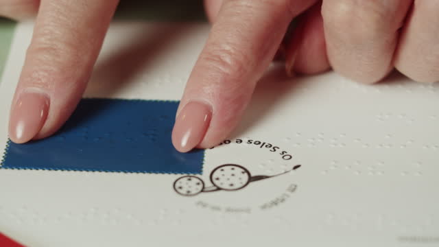 Blind woman reading postcard, braille, using fingers close-up, poorly seeing female person learning to read, home education for people with disabilities, touching letters on sheet of paper.
