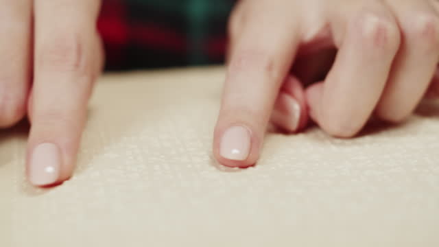 Blind woman reading braille book close-up, poorly seeing female person learning to read, home education for people with disabilities, touching letters on sheet of paper.