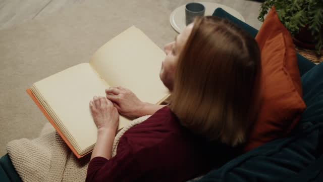 Blind woman reading braille book top view, poorly seeing female person learning to read, home education for people with disabilities, touching letters on sheet of paper.