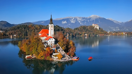Bled, Slovenia - October 31, 2018: Lake Bled with tourists in Pletna boat, castle and autumn colorful trees background
