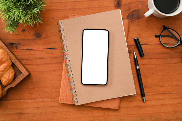 istock Workspace with smartphone white screen mockup on wood surface background. 1388489504
