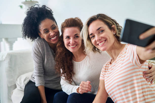 istock Female friends sitting on couch while taking selfie with smart phone 1388493043