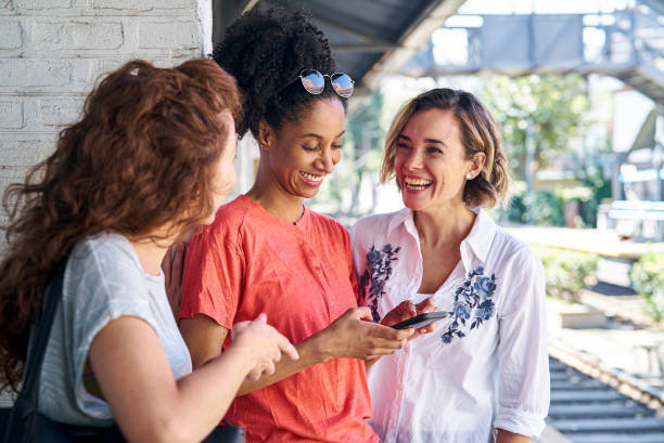istock Female friends laughing over smart phone while standing in train station 1388493154