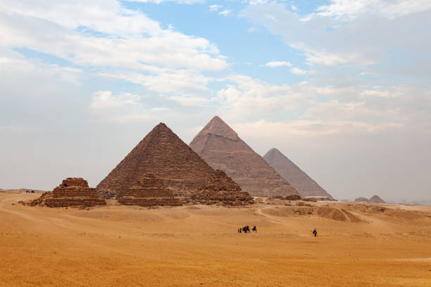 view of the giza plateau with tourists and native people riding camel and the great pyramid in the background. - egypt camel pyramid shape pyramid imagens e fotografias de stock