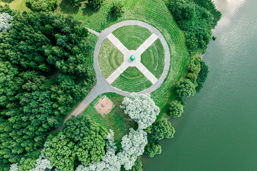 aerial top view from flying drone of a city park with walking path among green trees in sunny day