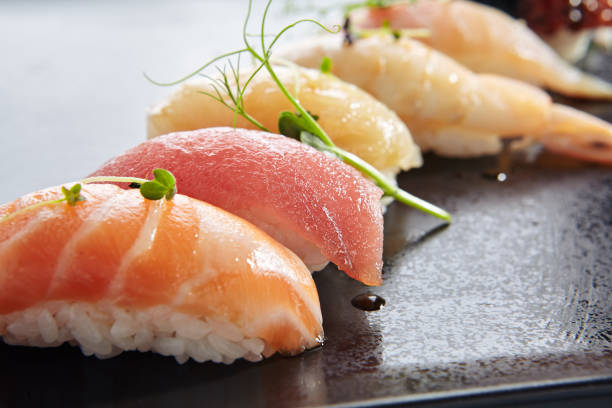 japanese nigiri sushi set - sushi with rice and various seafood. salmon, tuna, sea scallop and other seafood fish. nigiri sushi row on black slate platter. isolated on white background. - nigiri fotos stockfoto's en -beelden