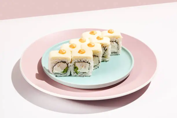 Photo of Alternative sushi roll with cheese outside, chicken inside, spicy sauce topped. Cheese maki in minimal style. Modern japanese menu concept. Chicken maki roll on ceramic plate on coloured background.