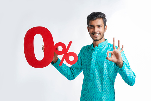 Indian man holding zero percent sign board promoting offers on festival season while wearing traditional cloths, standing over white background.