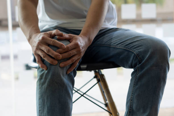 男は椅子に座り、痛みで膝をつかんでいた。変形性関節症の医学的概念に苦しむ - ラップドレス ストックフォトと画像