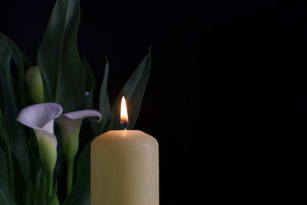 Candle burning flame in the darkness and arum lilies stock photo