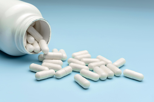 The medicine is poured out of the vial. Medicine capsules close-up on a blue background.