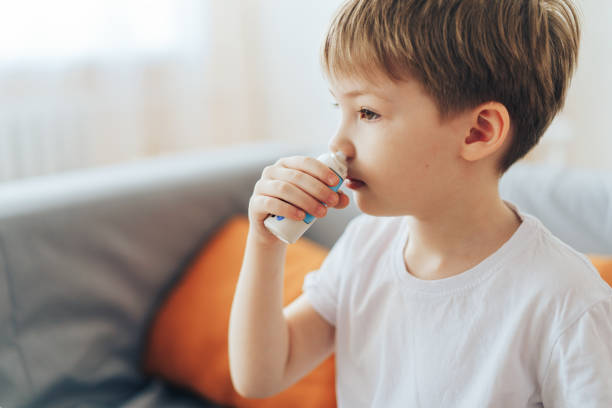 Little boy uses hormonal nasal spray while sitting on the couch stock photo