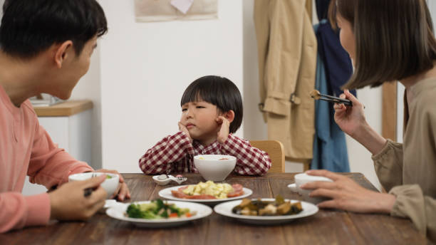 istock picky Asian boy shaking head while refusing food his father and mother put in his bowl during lunch time in dining room at home 1388510635