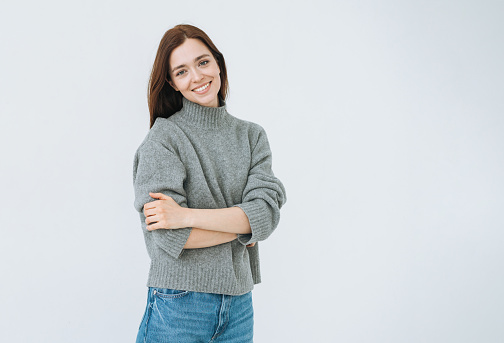 Happy emotional young woman with dark long hair in grey knitted swaeter on white background isolated