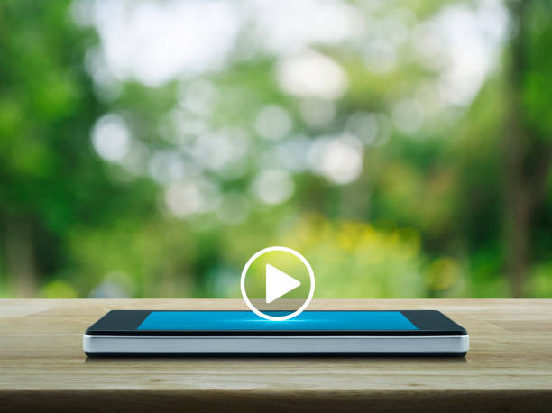 Play button flat icon on modern smart mobile phone screen on wooden table over blur green tree in park, Business music online concept