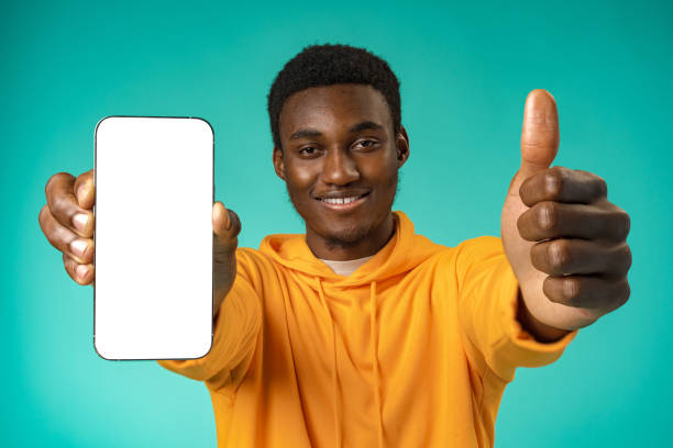 istock Smiling casual black man pointing at blank white cell phone screen in studio 1388512156