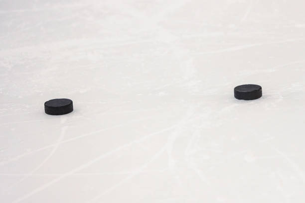 Two black pucks laying on ice hockey rink. Photo taken inside ice hockey rink before training.