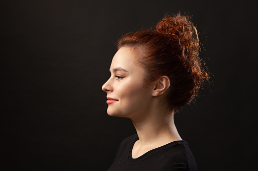 Close-up studio portrait of an attractive 20 year old red-haired woman in a black t-shirt on a black background