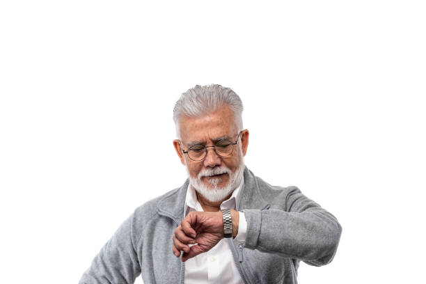 An elderly stylish man gray-haired and with a beard on a white isolated background looks at his watch. The concept of punctuality and discipline. High quality photo