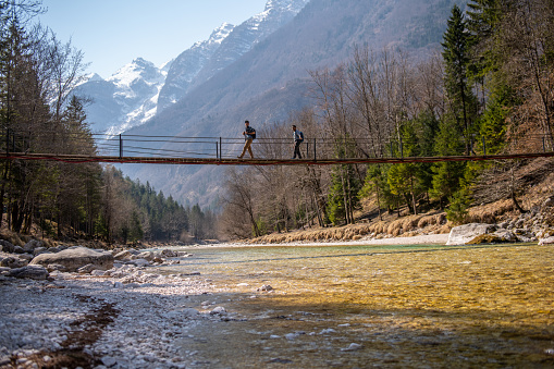 Hikers crossing the suspension bridge over Soca river in Julian Alps, Slovenia, Europe.