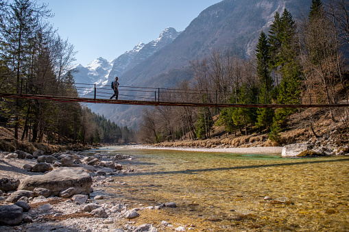 Hiker crossing the suspension bridge over Soca river in Julian Alps, Slovenia, Europe.