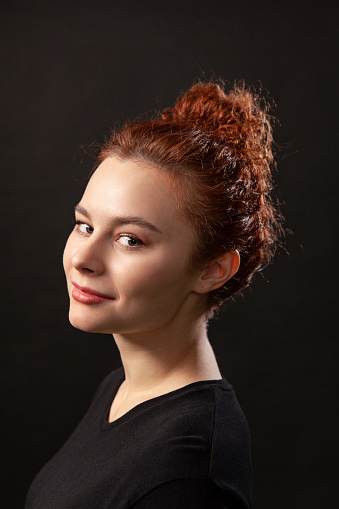Close-up studio portrait of an attractive 20 year old red-haired woman in a black t-shirt on a black background