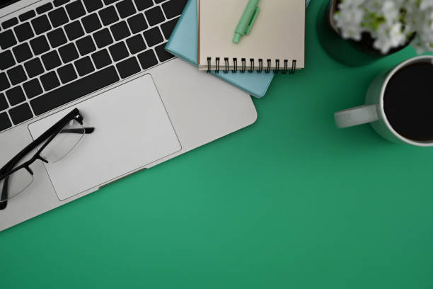 istock Above view computer laptop, eyeglasses, notebook and coffee cup on green background. 1388520787