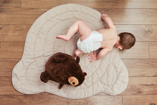 Falling infant baby boy in diapers while crawling or walking. Child first steps and fall to the floor, top view