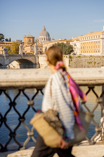 Woman walking on the bridge in Rome on a sunny autumn day. Elegant woman wearing stripped blouse and shawl in hair. Focus on background