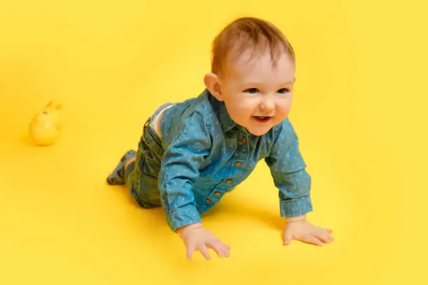 A happy child on a studio yellow background in a blue shirt and pants. Smiling infant baby boy in jeans