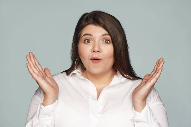 foto aislada de una joven de talla grande con ojos de insecto emocional con camisa blanca formal, expresando asombro, exclamando emocionada, gesticulando sorprendentemente, sus ojos llenos de incredulidad y asombro. - raised eyebrows women human face thinking fotografías e imágenes de stock