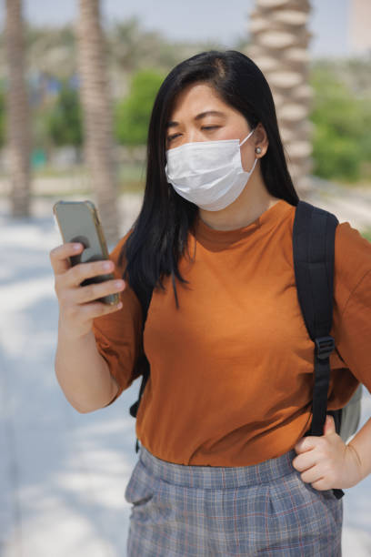 istock Young woman with protective face mask using video call mobile app on city break 1388529300