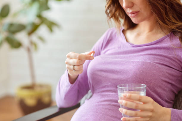 Pregnant woman taking pill at home Close up of a serious pregnant woman holding a pill and a glass of water. prenatal vitamin, medication for healthy pregnancy folic acid stock pictures, royalty-free photos & images